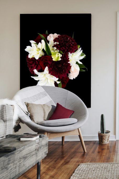 Framed artwork featuring a vibrant bouquet of red, white, and blush flowers on a black background, displayed in a modern living space.