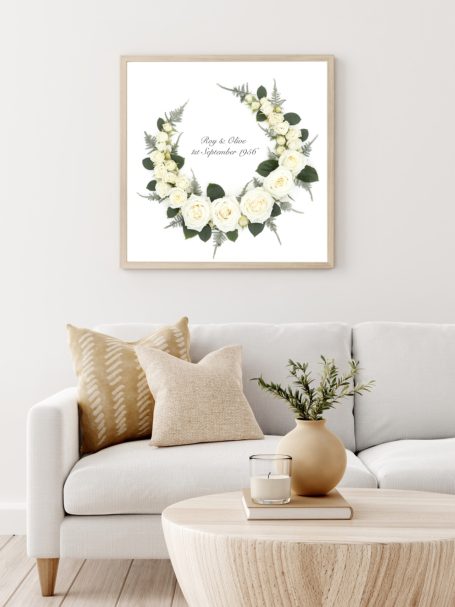 Elegant floral preservation artwork featuring a wreath of white roses and greenery, framed above a neutral modern sofa.